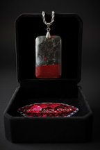 African Bloodstone pendant necklace on a rope chain in a black velvet jewelry box on a dark background.