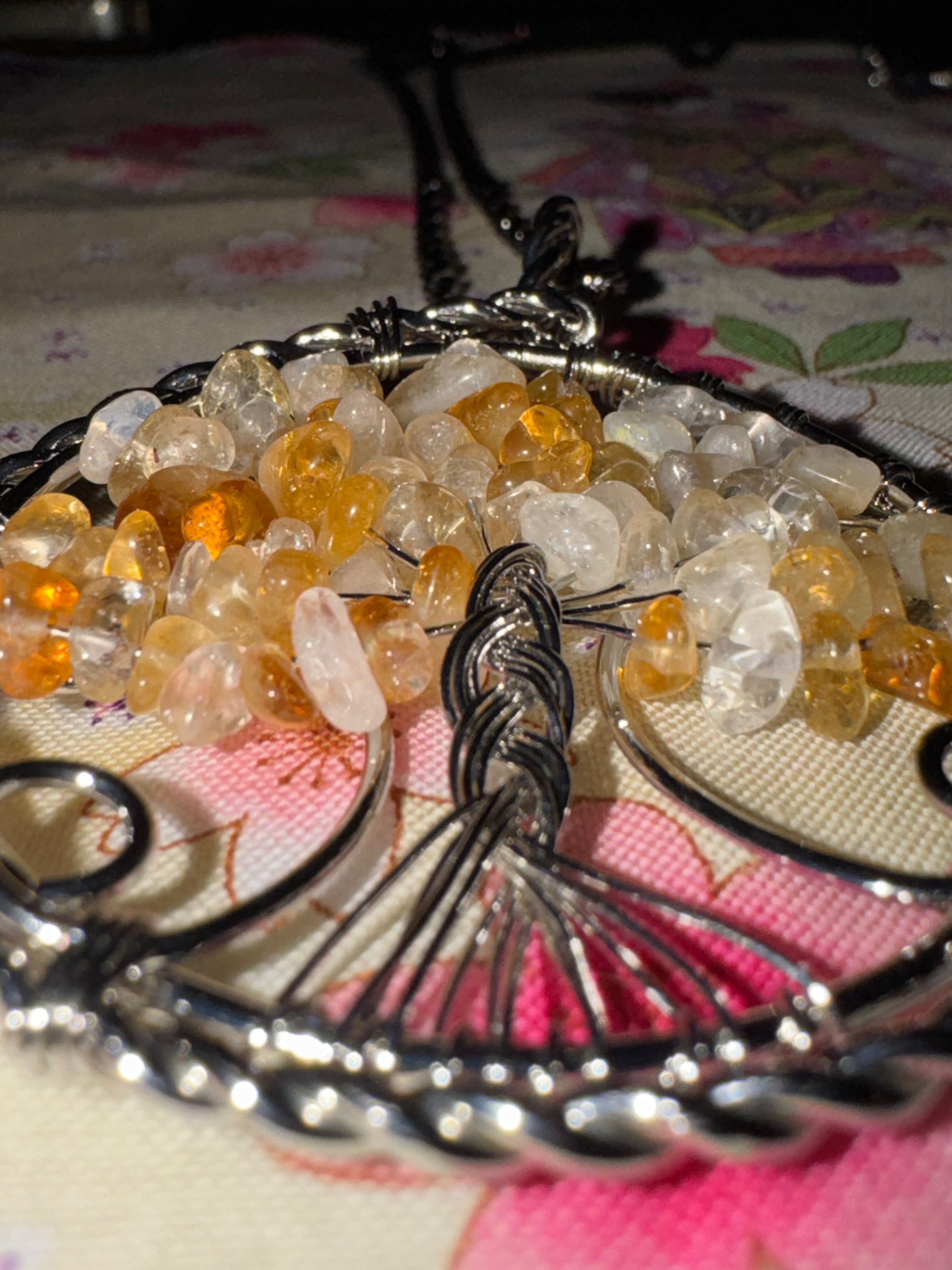 Close-up of a wire wrapped Royal tangerine quartz tree of life pendant on a floral fabric background