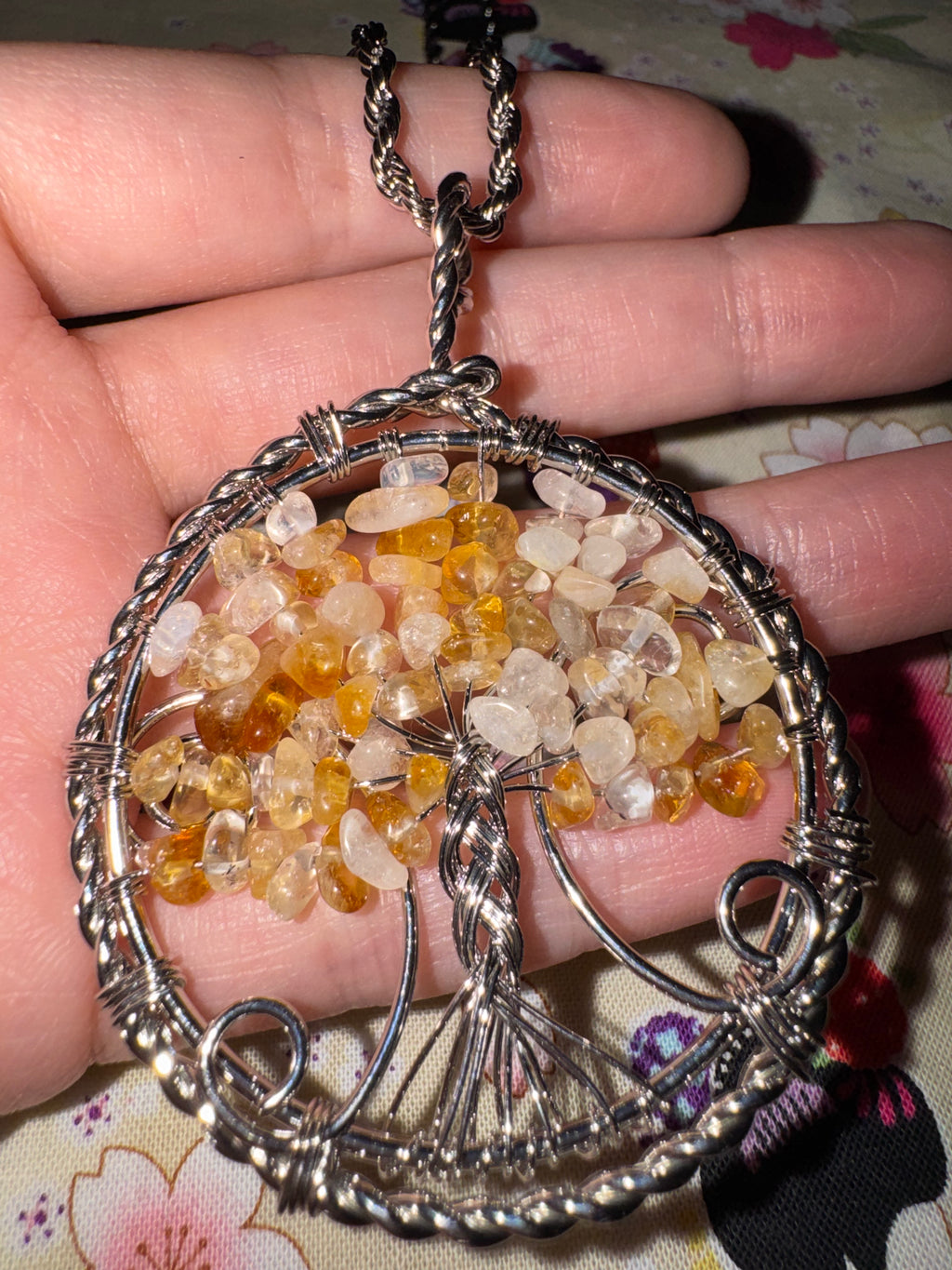 A wire wrapped Royal tangerine quartz tree of life pendant held in hand on a floral fabric background