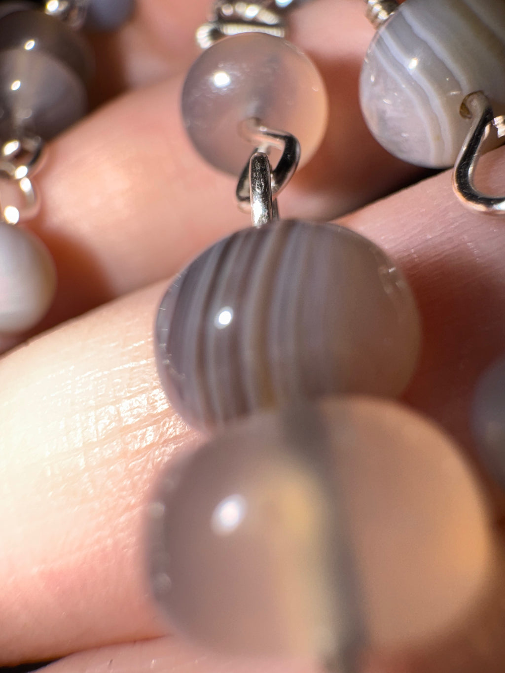 Close-up of a botswana agate beaded necklace with gray beads and silver chain on a hand.