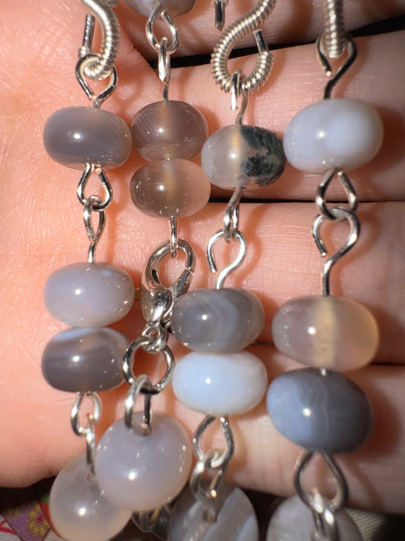 Close-up of a botswana agate beaded necklace with gray beads and silver chain on a hand.