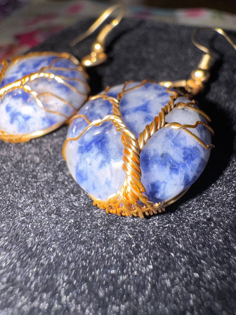 Blue sodalite stone earrings with gold wire wrapping on a dark surface