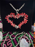 A hand-crafted red coral, heart-shaped stainless steel pendant necklace on a dark fabric background in a gothic setting.