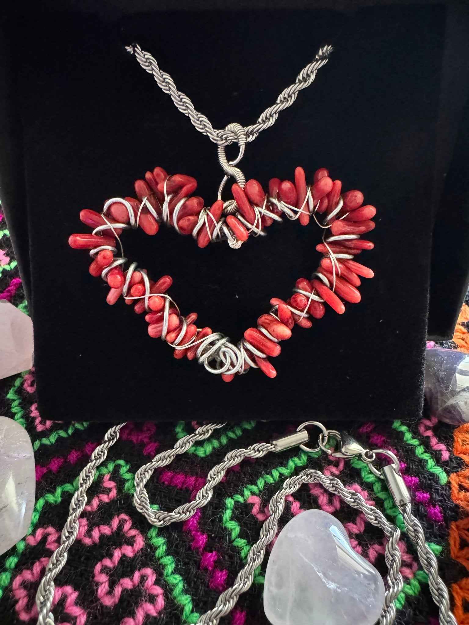 A hand-crafted red coral, heart-shaped stainless steel pendant necklace on a dark fabric background in a gothic setting.