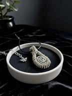 A reversible wire wrapped moonstone pendant with a swirly design on a dish with a dark background in a dark naturalism aesthetic.