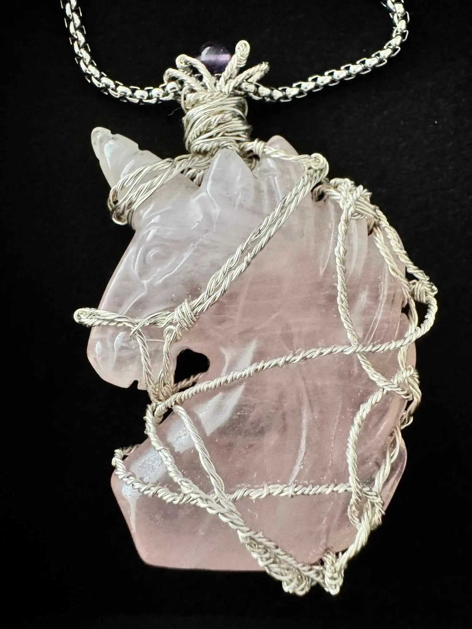Wire wrapped rose quartz unicorn pendant necklace on a dark background